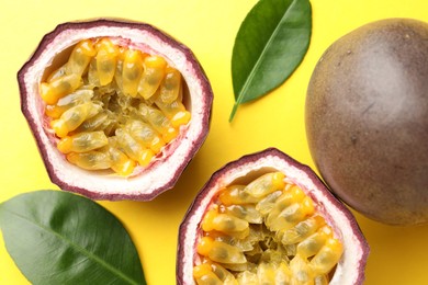Photo of Fresh passion fruits with green leaves on yellow background, closeup
