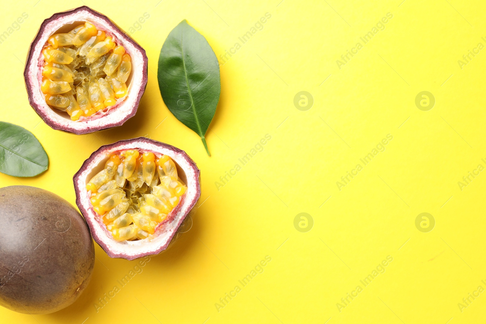 Photo of Fresh passion fruits with green leaves on yellow background, flat lay. Space for text