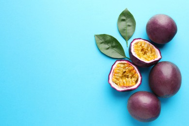 Photo of Fresh passion fruits with green leaves on light blue background, flat lay. Space for text