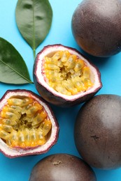 Photo of Fresh passion fruits with green leaves on light blue background, above view