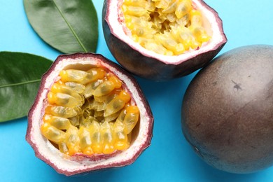 Photo of Fresh passion fruits with green leaves on light blue background, closeup