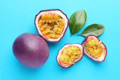 Photo of Fresh passion fruits with green leaves on light blue background, flat lay
