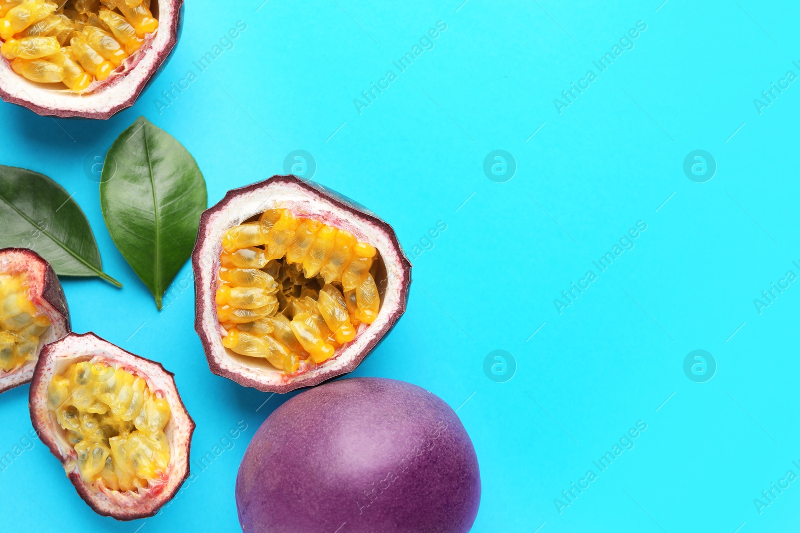 Photo of Fresh passion fruits with green leaves on light blue background, flat lay. Space for text
