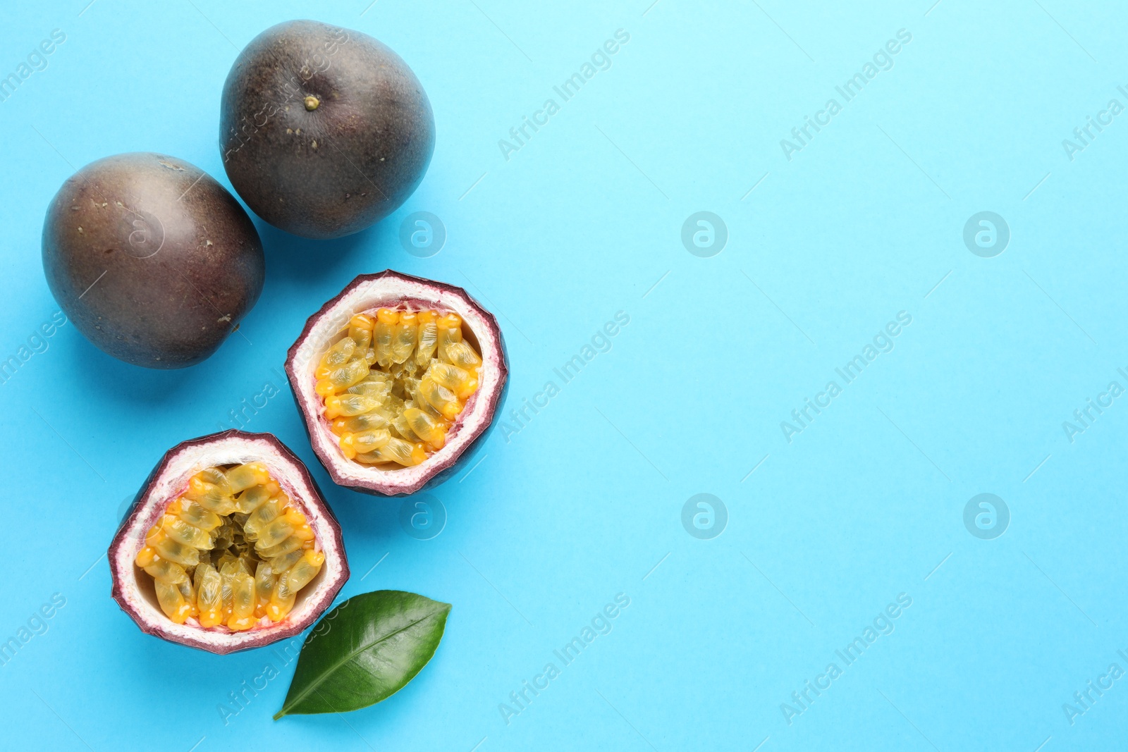 Photo of Fresh passion fruits with green leaf on light blue background, flat lay. Space for text