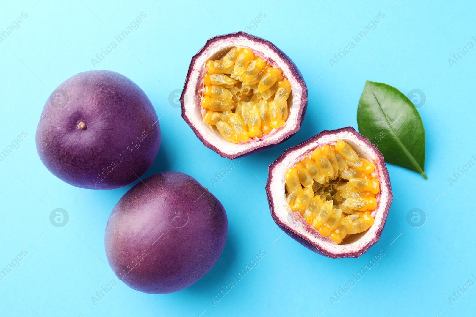 Photo of Fresh passion fruits with green leaf on light blue background, flat lay