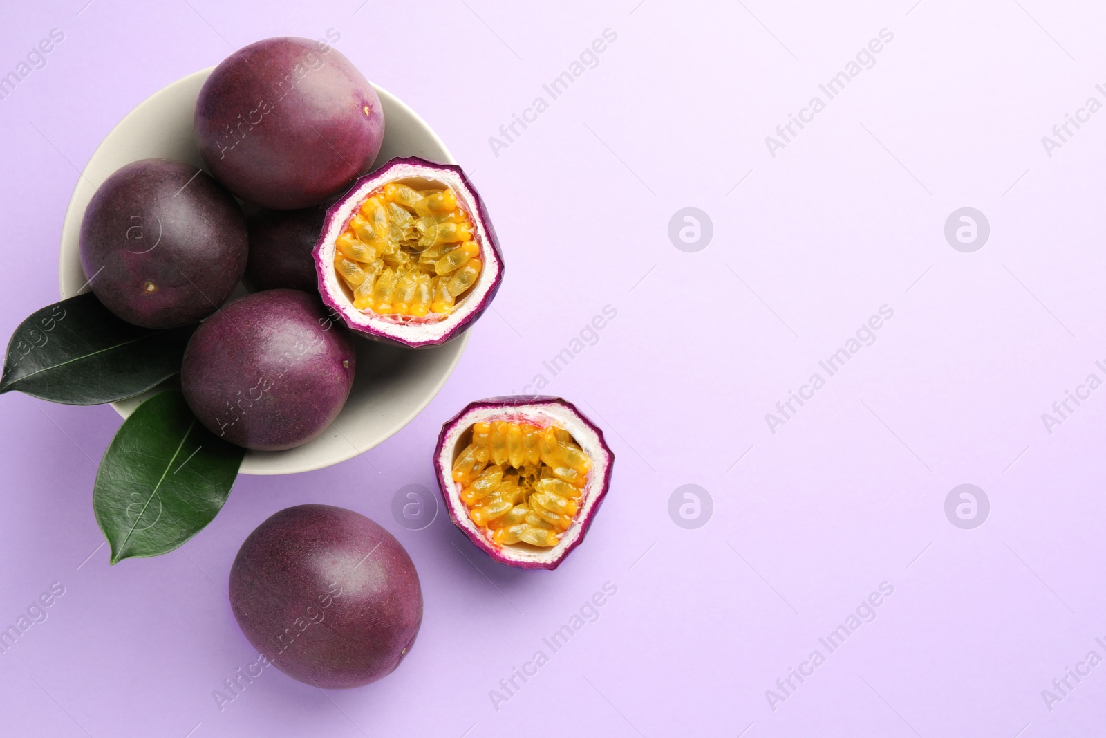 Photo of Fresh passion fruits with green leaves on violet background, flat lay. Space for text