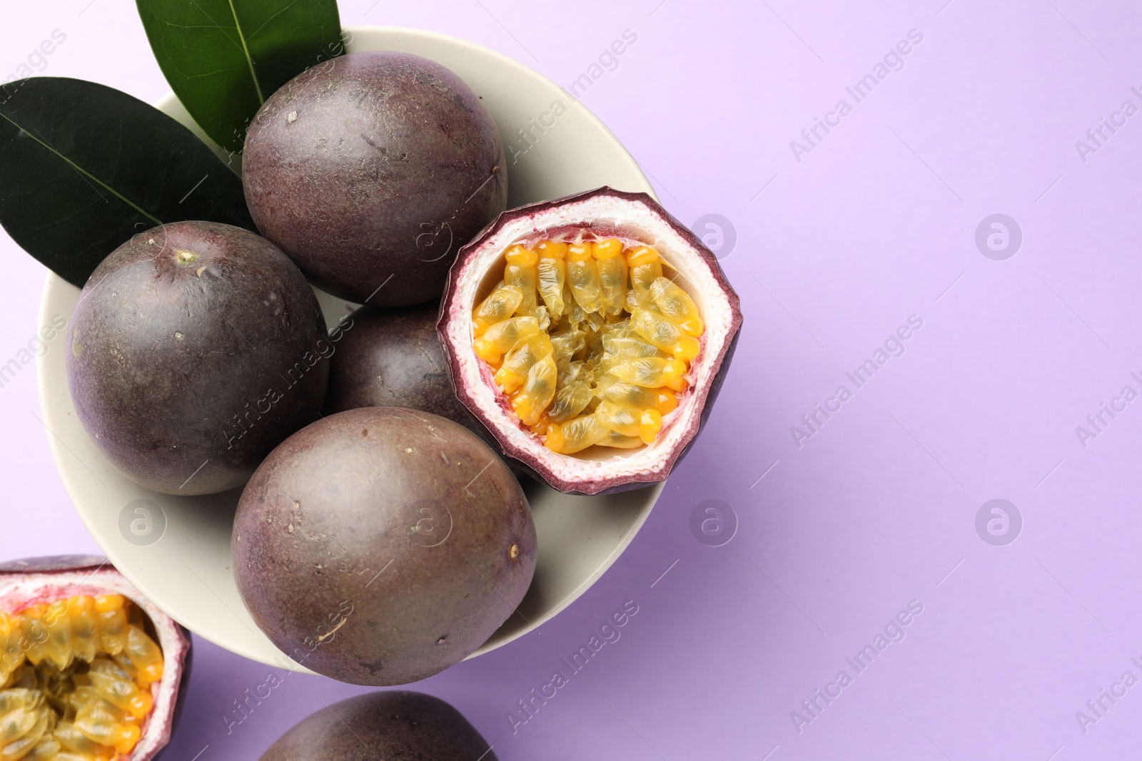 Fresh passion fruits with green leaves on violet background, flat lay. Space for text Photo of Fresh passion fruits with green leaves on violet background, flat lay. Space for text