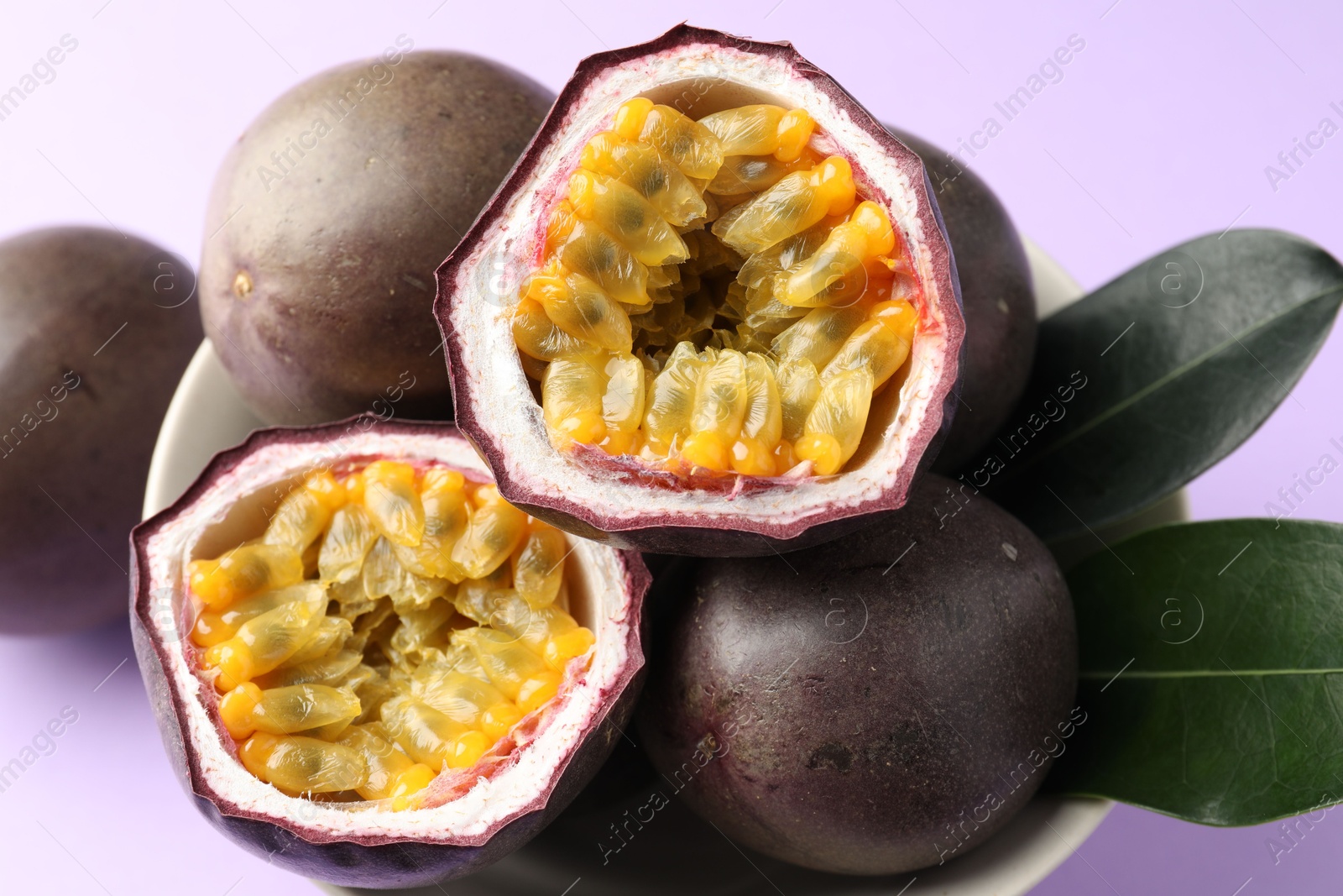 Photo of Fresh passion fruits with green leaves on violet background, closeup