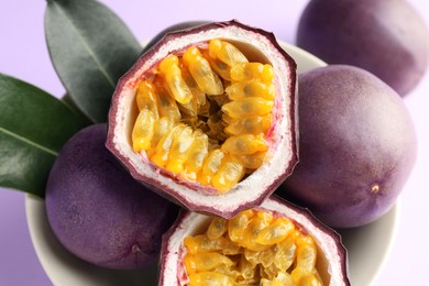 Photo of Fresh passion fruits with green leaves on violet background, closeup