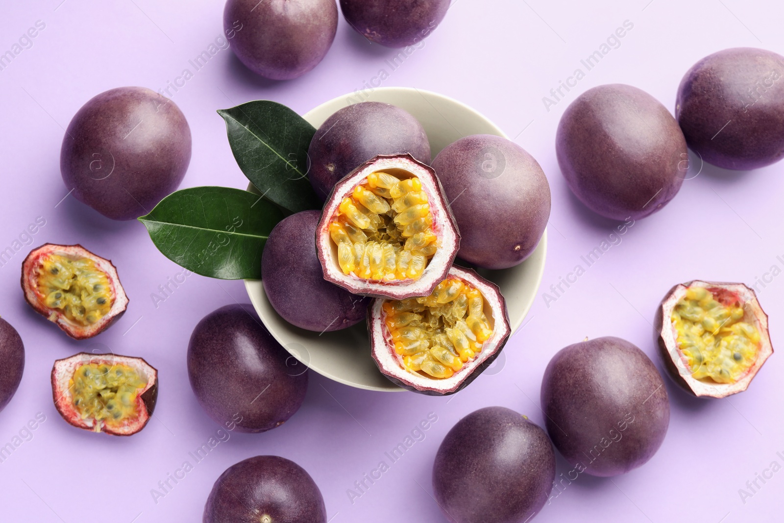 Photo of Fresh passion fruits with green leaves on violet background, flat lay