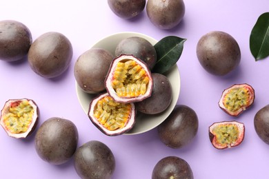 Photo of Fresh passion fruits with green leaves on violet background, flat lay