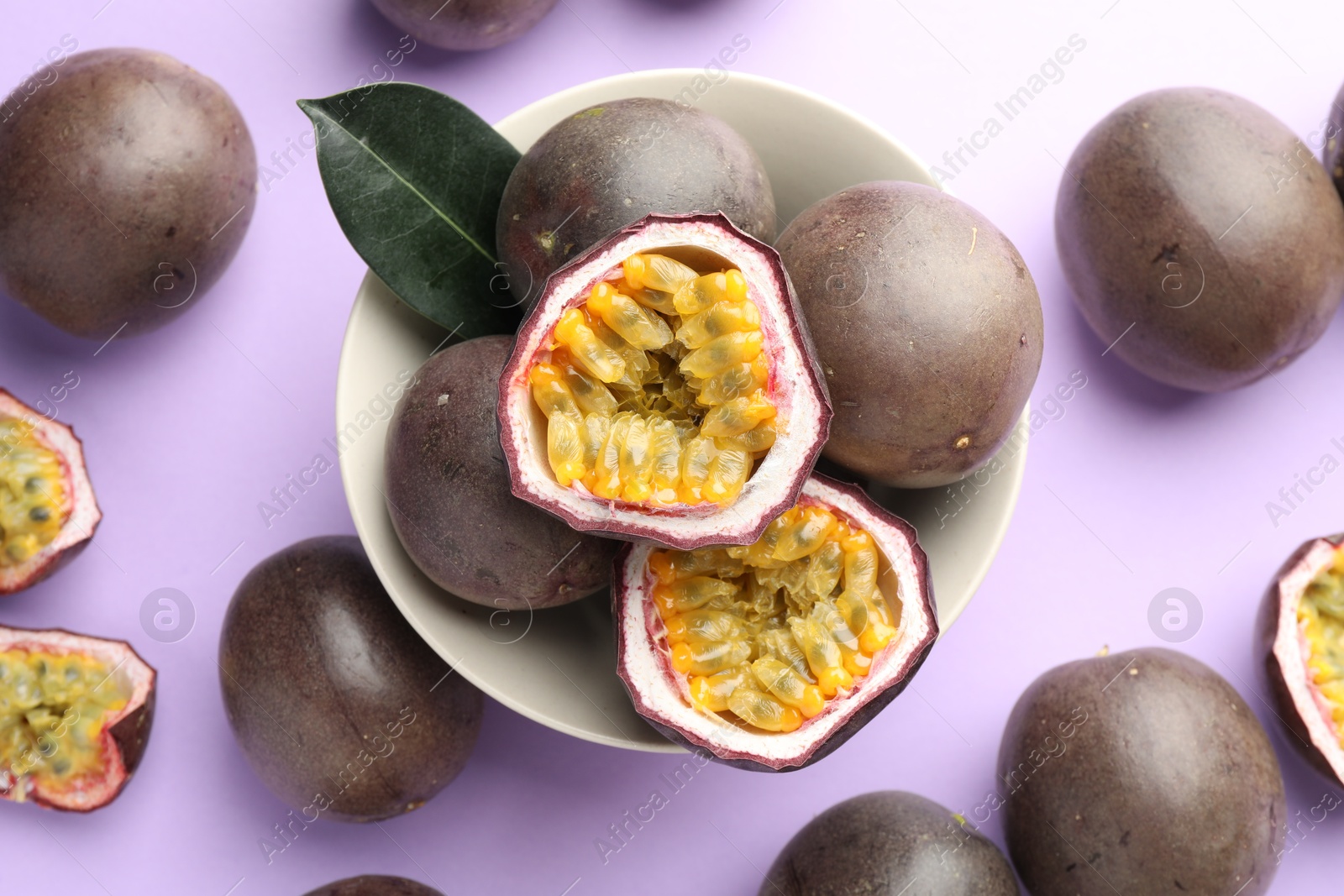 Photo of Fresh passion fruits with green leaf on violet background, above view