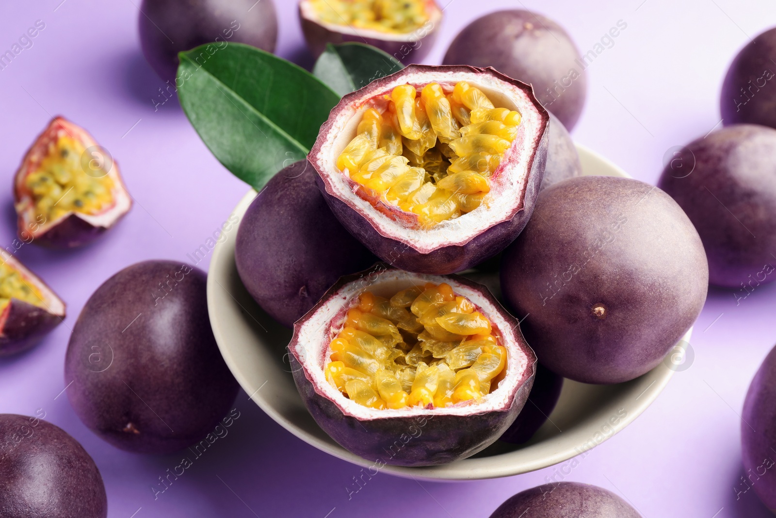 Fresh passion fruits with green leaves on violet background, closeup Photo of Fresh passion fruits with green leaves on violet background, closeup