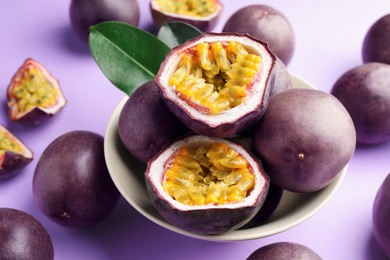 Photo of Fresh passion fruits with green leaves on violet background, closeup