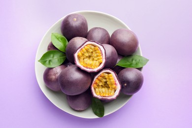 Photo of Fresh passion fruits with green leaves on violet background, top view