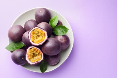 Photo of Fresh passion fruits with green leaves on violet background, top view. Space for text