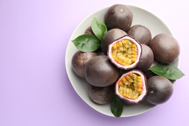 Photo of Fresh passion fruits with green leaves on violet background, top view. Space for text