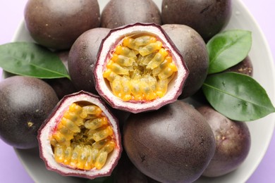 Photo of Fresh passion fruits with green leaves on violet background, closeup