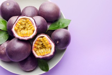 Photo of Fresh passion fruits with green leaves on violet background, above view. Space for text