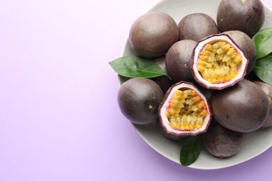 Photo of Fresh passion fruits with green leaves on violet background, above view. Space for text