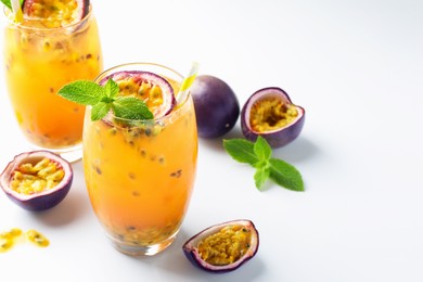 Photo of Tasty passion fruit drink with mint in glasses and fresh fruits on white table