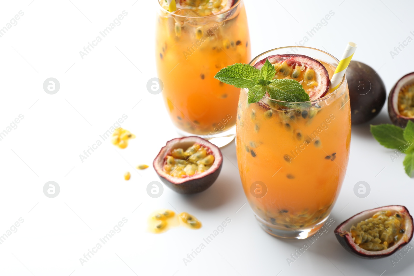 Photo of Tasty passion fruit drink with mint in glasses and fresh fruits on white table, closeup. Space for text