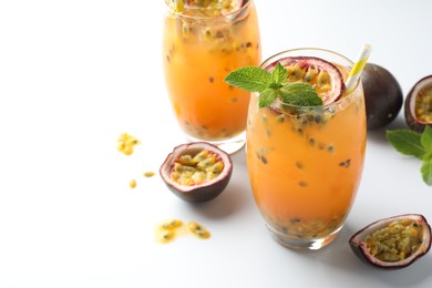 Photo of Tasty passion fruit drink with mint in glasses and fresh fruits on white table, closeup. Space for text