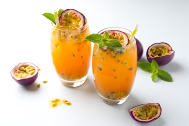 Photo of Tasty passion fruit drink with mint in glasses and fresh fruits on white table