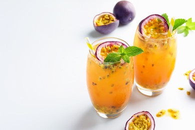 Photo of Tasty passion fruit drink with mint in glasses and fresh fruits on white table. Space for text