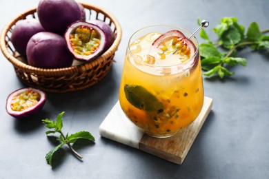 Photo of Tasty passion fruit drink in glass, fresh fruits and mint on gray table, closeup