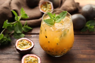 Photo of Tasty passion fruit drink with mint in glass and fresh fruits on wooden table, closeup