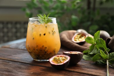 Photo of Tasty passion fruit drink with mint in glass and fresh fruits on wooden table, closeup