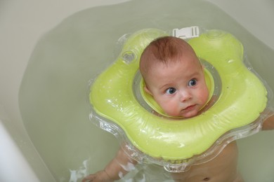 Photo of Cute little baby swimming with inflatable ring in bath, above view