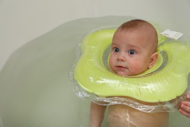 Photo of Cute little baby swimming with inflatable ring in bath