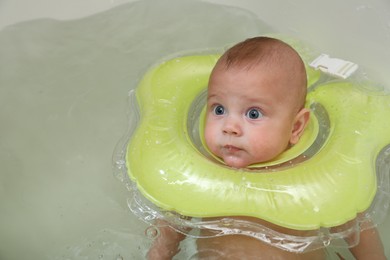 Photo of Cute little baby swimming with inflatable ring in bath