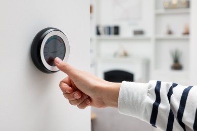 Photo of Woman adjusting hygrometer on white wall indoors, closeup. Smart home system
