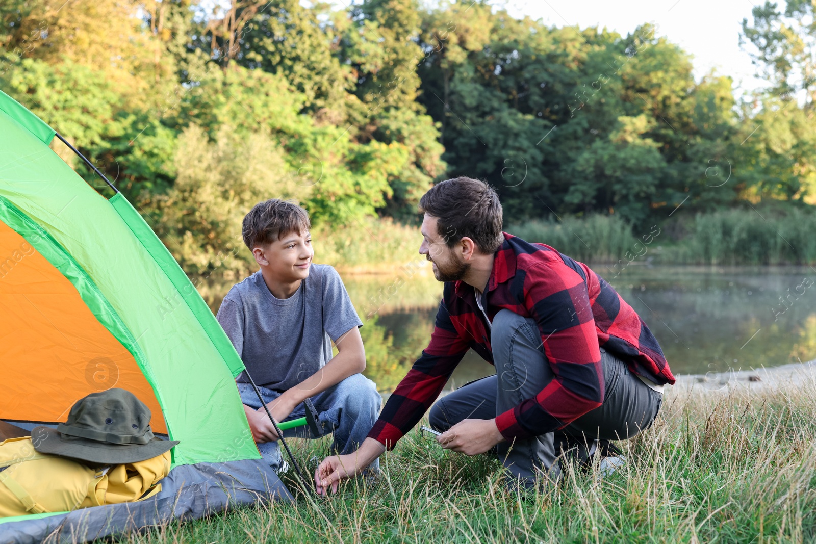 Photo of Happy father and son setting up camping tent near river outdoors