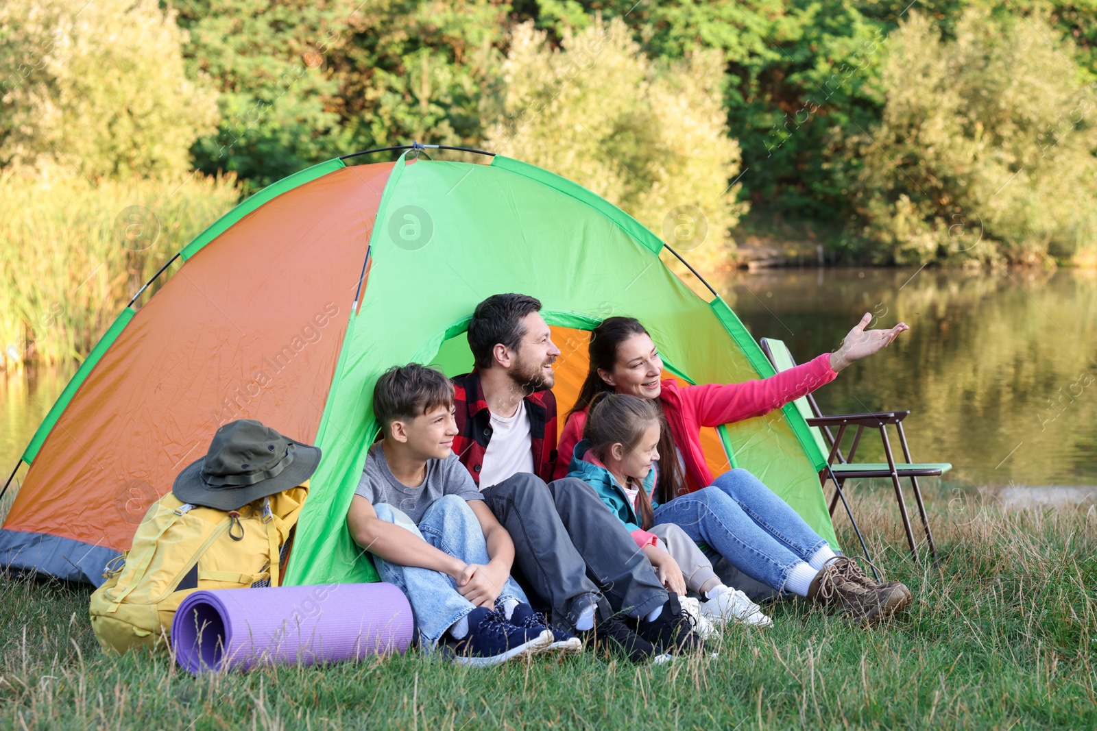 Photo of Happy family spending time together with camping tent and tourist equipment near river outdoors