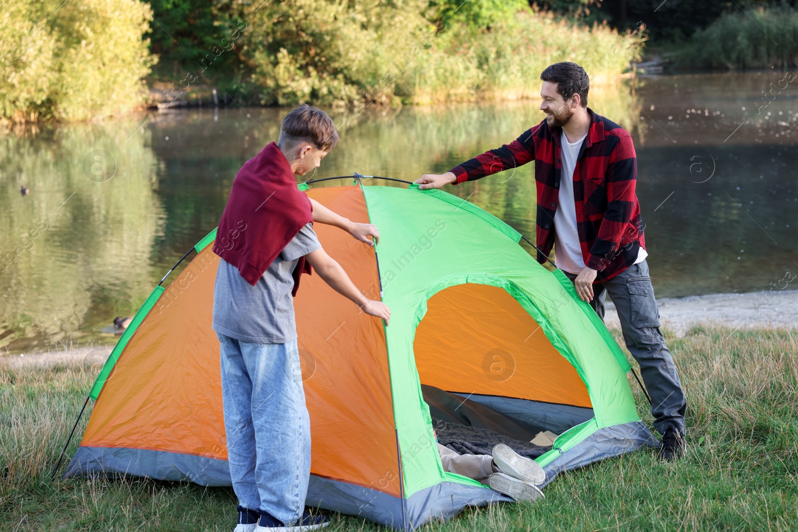 Photo of Happy father and son setting up camping tent near river outdoors