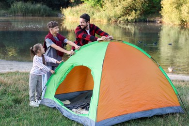 Photo of Happy father and his children setting up camping tent near river outdoors
