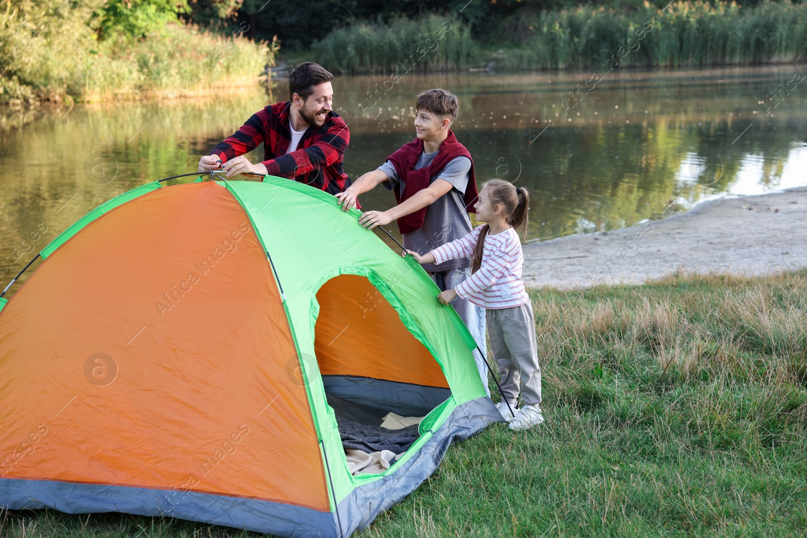 Happy father and his children setting up camping tent near river outdoors. Space for text Photo of Happy father and his children setting up camping tent near river outdoors. Space for text