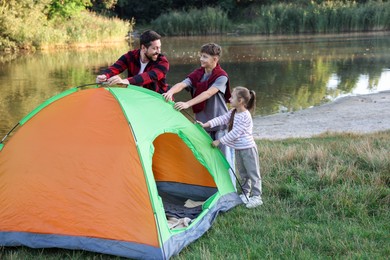 Photo of Happy father and his children setting up camping tent near river outdoors. Space for text