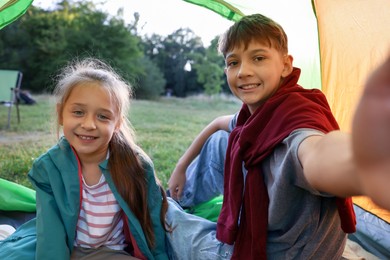Photo of Happy brother and sister taking selfie in camping tent outdoors