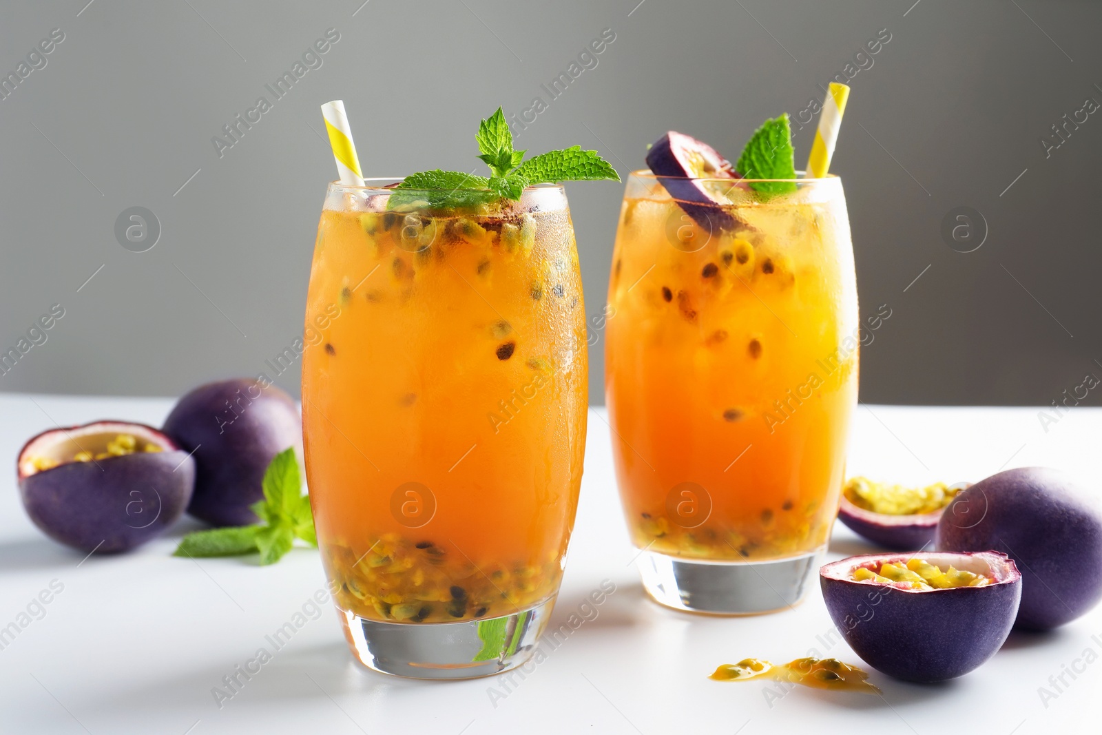 Photo of Tasty passion fruit drink with mint in glasses and fresh fruits on light table against gray background