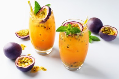 Photo of Tasty passion fruit drink with mint in glasses and fresh fruits on white table