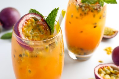 Photo of Tasty passion fruit drink with mint in glasses and fresh fruits on light table, closeup