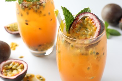 Photo of Tasty passion fruit drink with mint in glasses and fresh fruits on light table, closeup