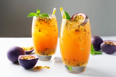 Photo of Tasty passion fruit drink with mint in glasses and fresh fruits on light table against gray background, closeup