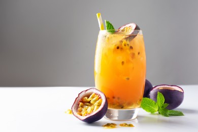 Photo of Tasty passion fruit drink with mint in glass and fresh fruits on light table against gray background, closeup