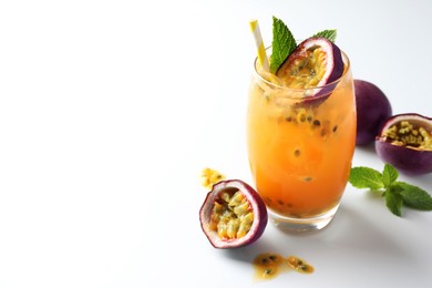 Photo of Tasty passion fruit drink with mint in glass and fresh fruits on white table, closeup. Space for text